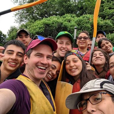 The 2019 cohort of participants smiling dressed in life-jackets getting ready for a canoe trip